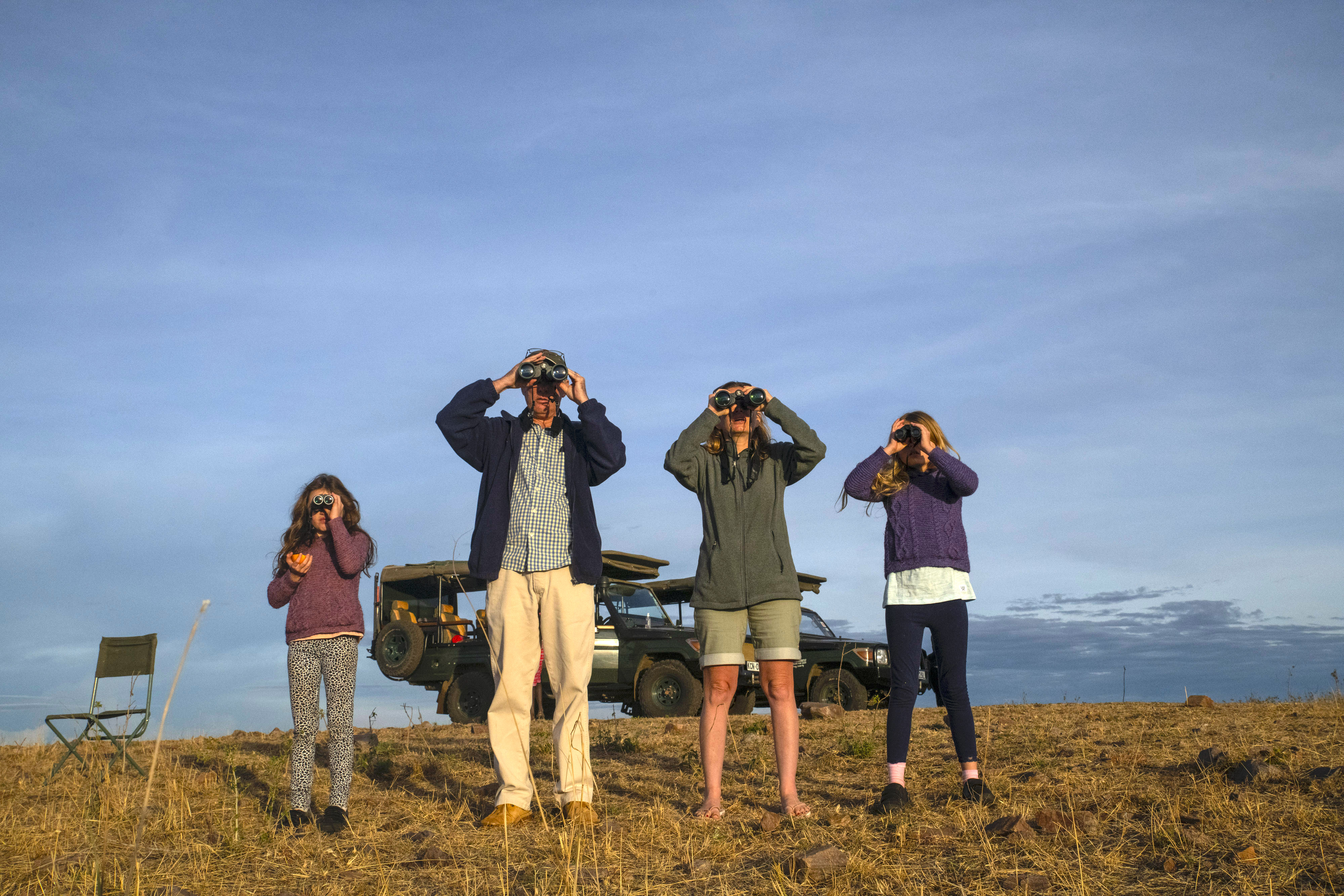 Family using binoculars to watch wildlife during a safari in the Maasai Mara.