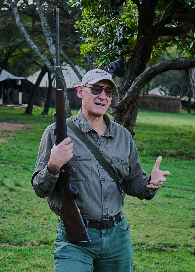 Calvin Cottar speaking to guests while holding a safari rifle at Cottar’s 1920s Camp.