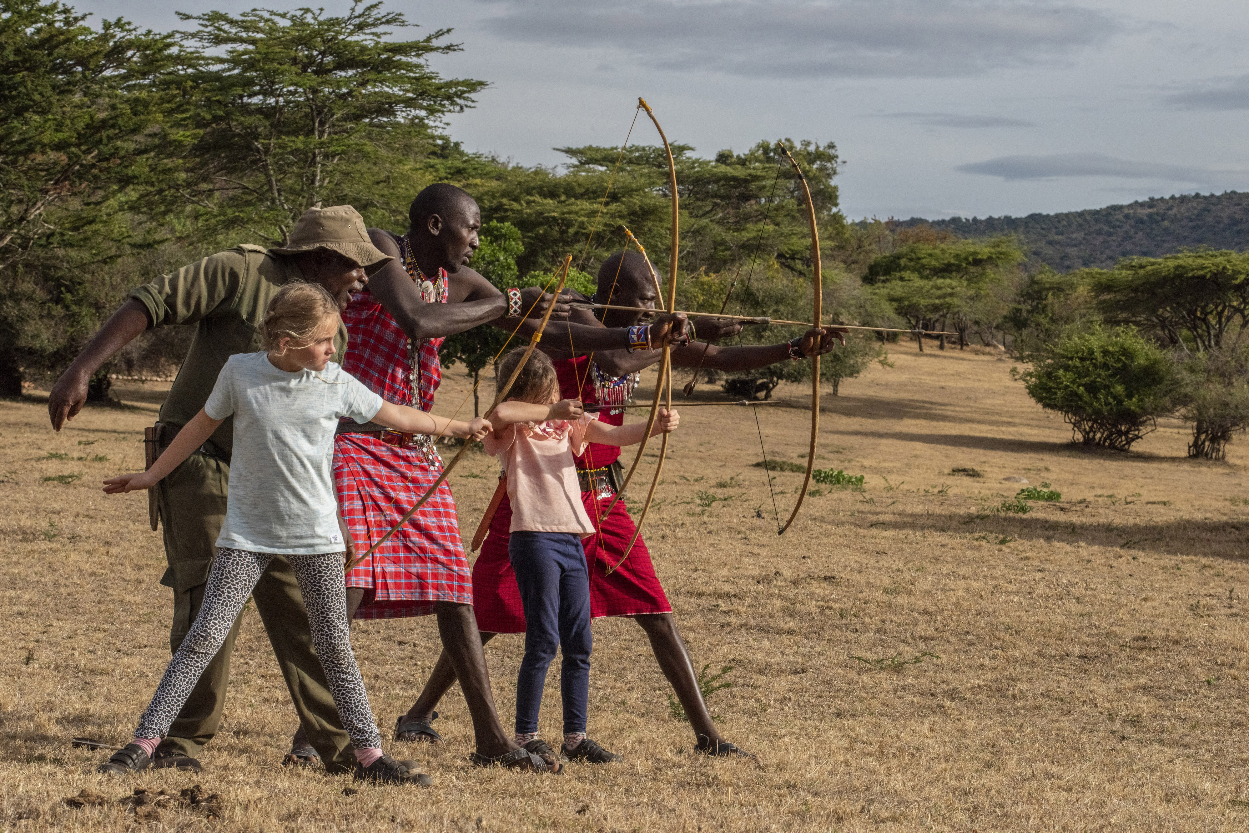 Children learning traditional Maasai archery with local guides during a family safari experience in Kenya.