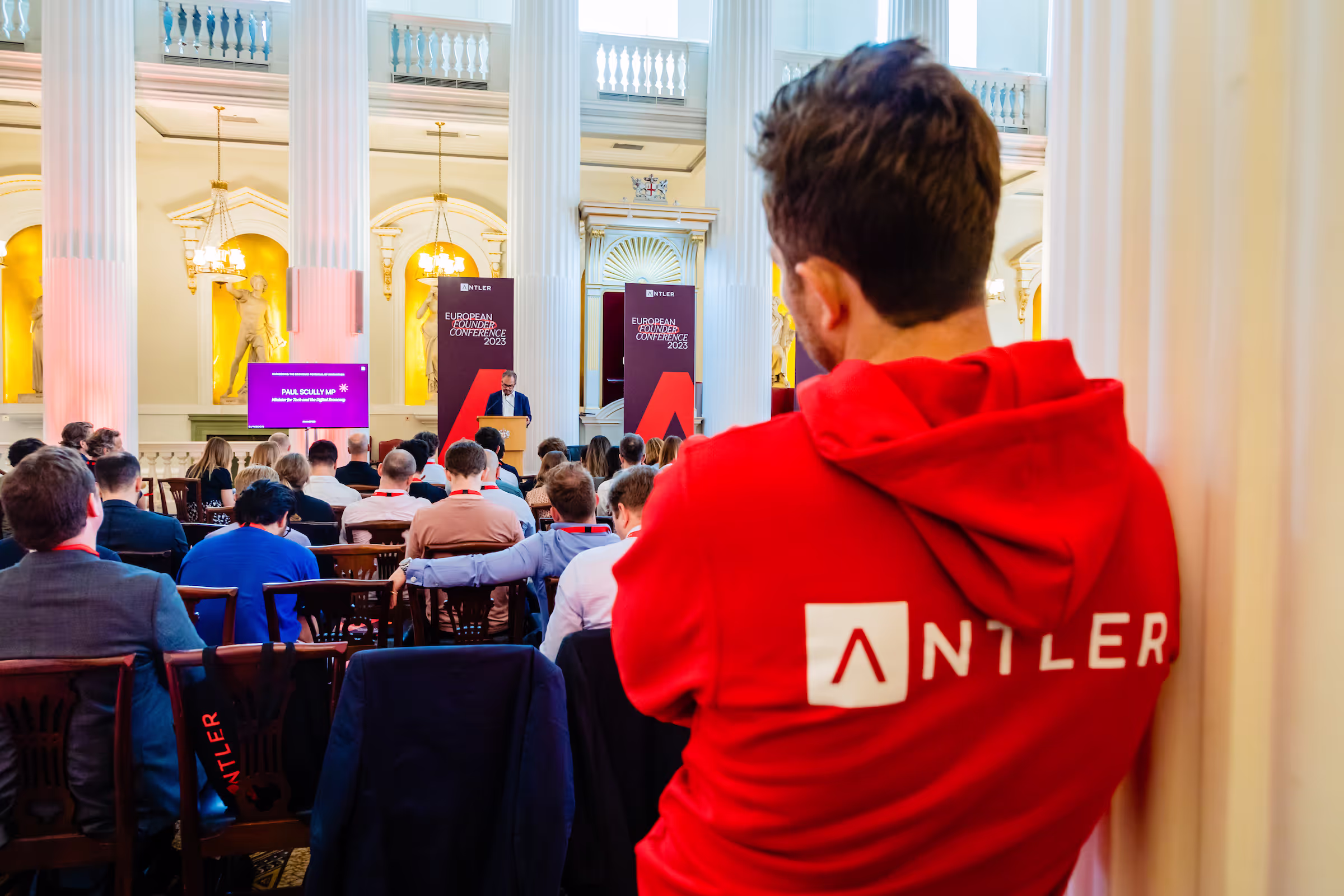 Antler founder watching an event wearing a red sweater