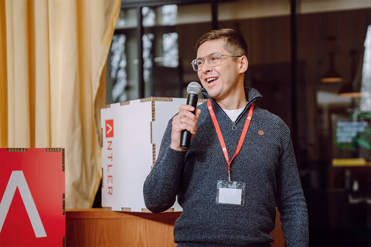 A man wearing a black sweater and glasses is speaking into a microphone.