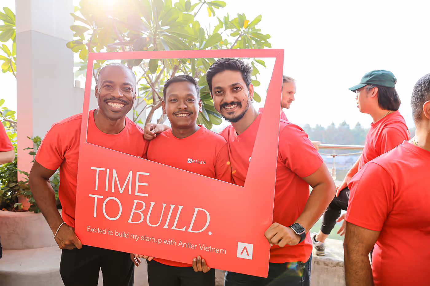 Three founders holding an Antler sign posing for photo wearing red shirts