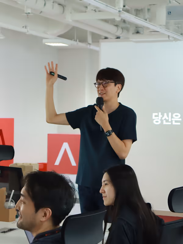 검은 셔츠를 입은 남자가 발표를 하고 있다.