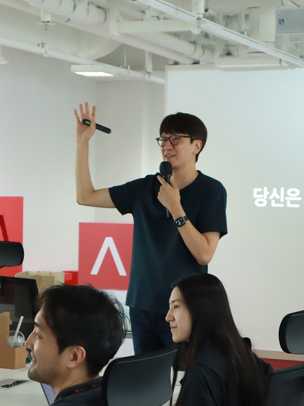 검은 셔츠를 입은 남자가 발표를 하고 있다.