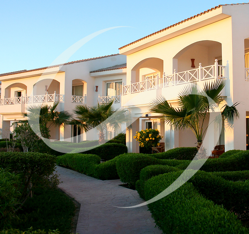 A white building with many balconies and bushes in front of it.