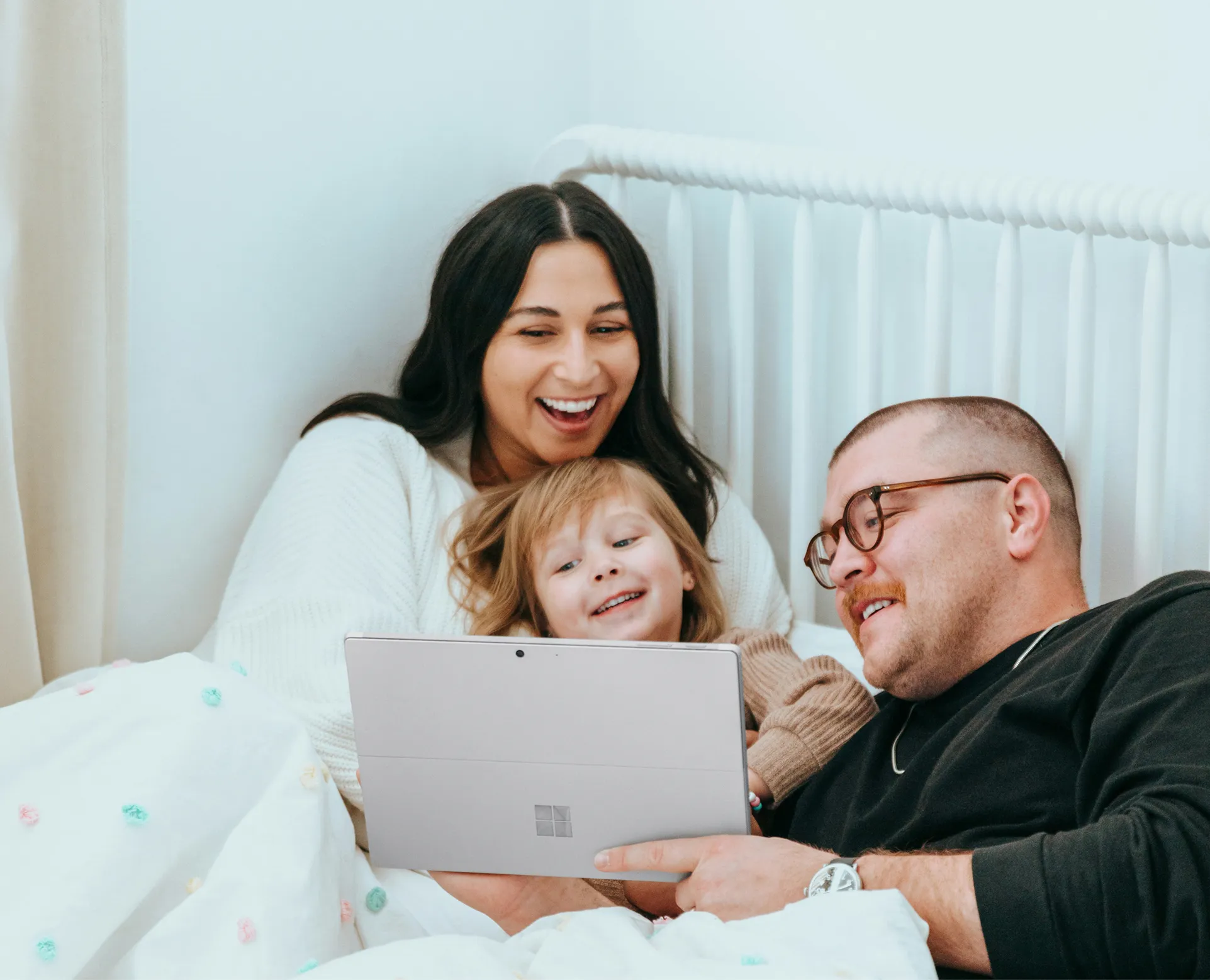 Smiling family of three lying on a bed watching a tablet together.
