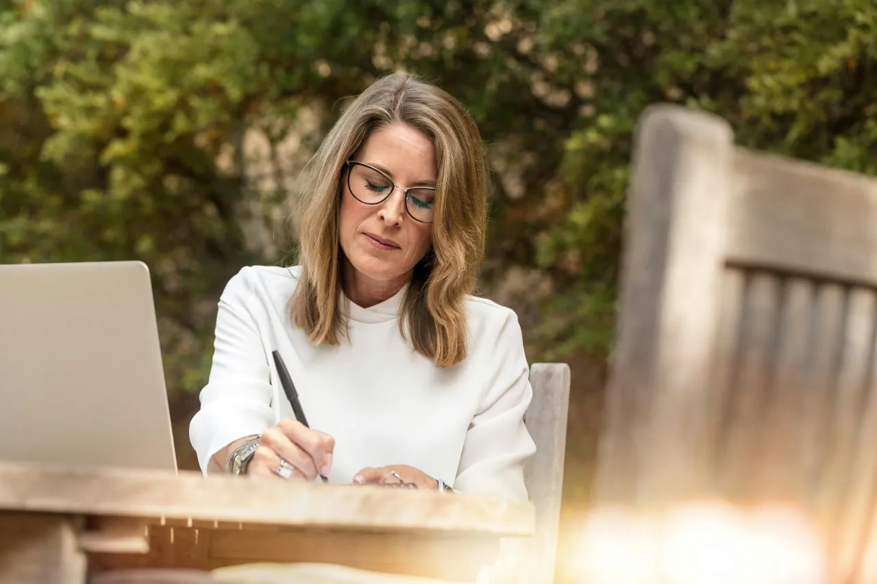Femme à lunettes prenant des notes à côté d'un ordinateur portable