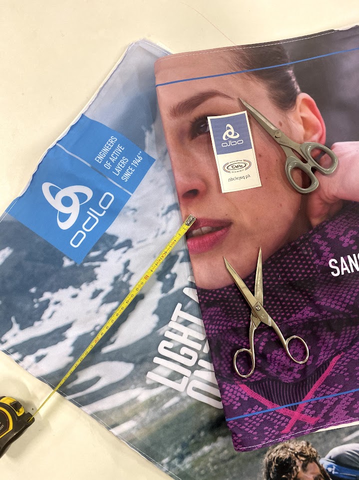 tissu imprimé pour support publicitaire en cours de découpe avec ciseaux et mètre ruban sur une table d’atelier