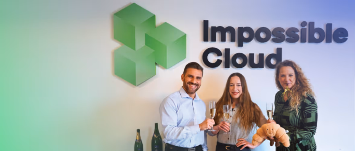 Impossible Cloud team members celebrating with champagne glasses in front of the Impossible Cloud logo