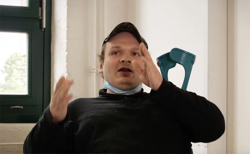 Mitglieder der Werkstatträte Deutschland winken beim Gruppenfoto in die Kamera. Im Hintergrund Bäume und ein buntes Gebäude.