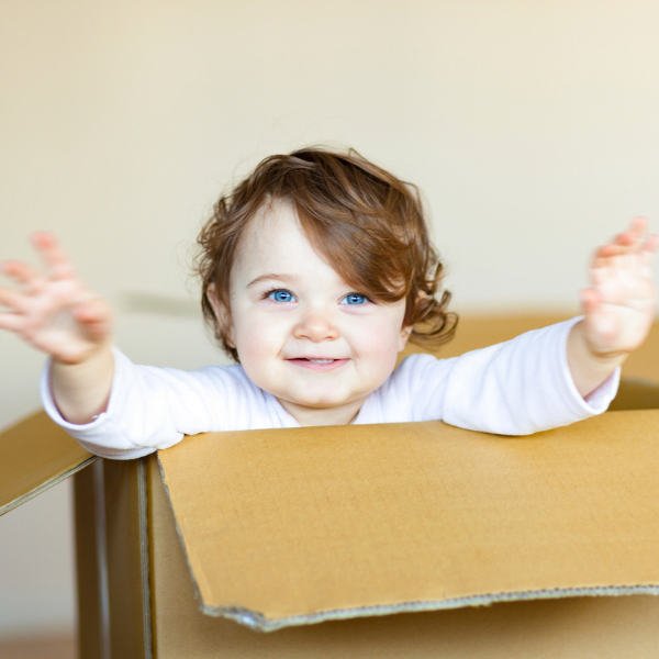 Smiley toddler waving in cardboard moving box