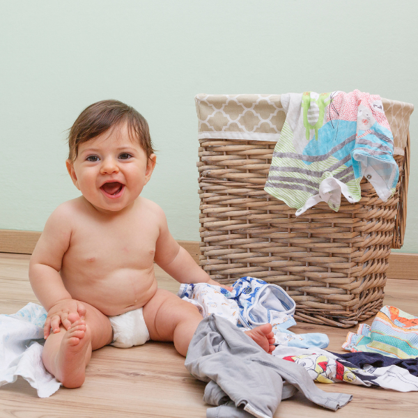 A cute baby sat by a washing basket full of clothes