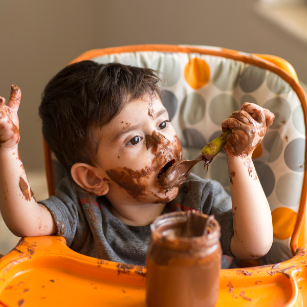 Small boy sat in highchair with chocolate spread all over him