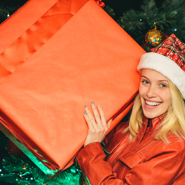 Woman wearingtartan Santa hat holding large orange Christmas box 