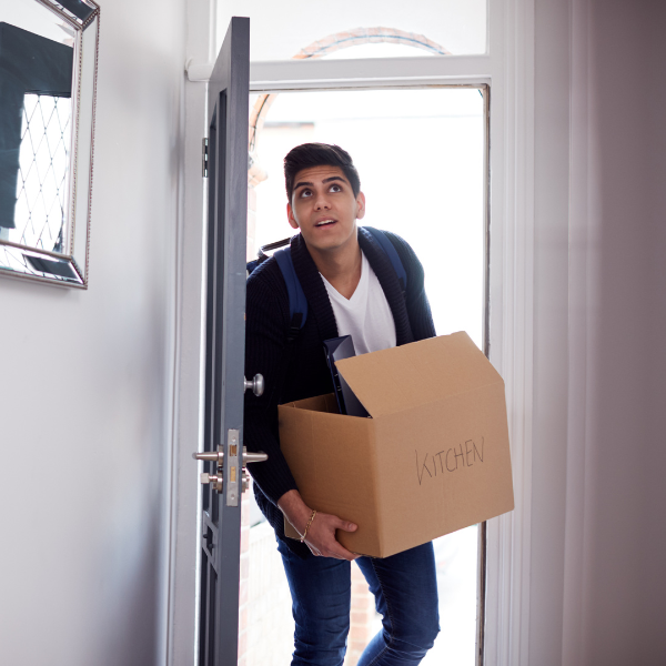 A young man walking in the front door of his new house with a moving box