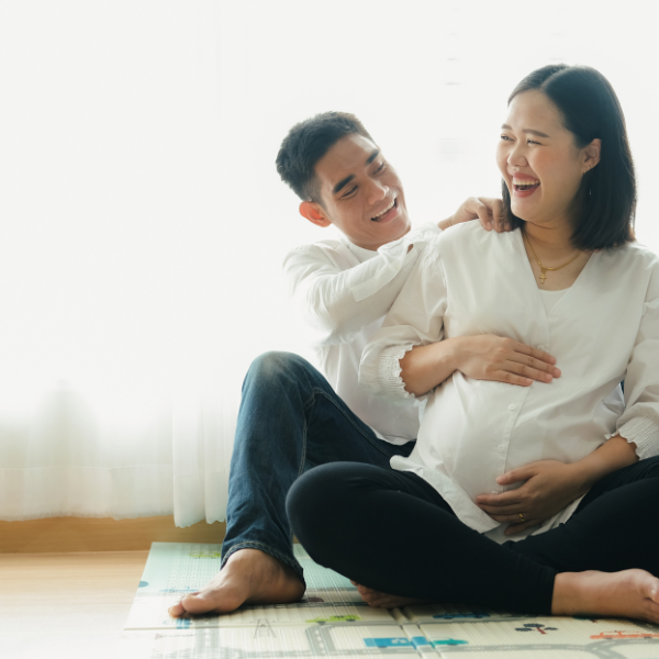 Pregnant couple man and woman sat on the floor laughing