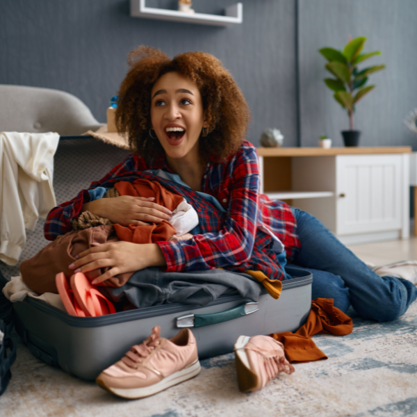 Woman laughing as she tries to lie on and close an overpacked suitcase