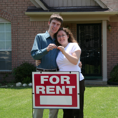 Happy couple outside house with keys and rental sign