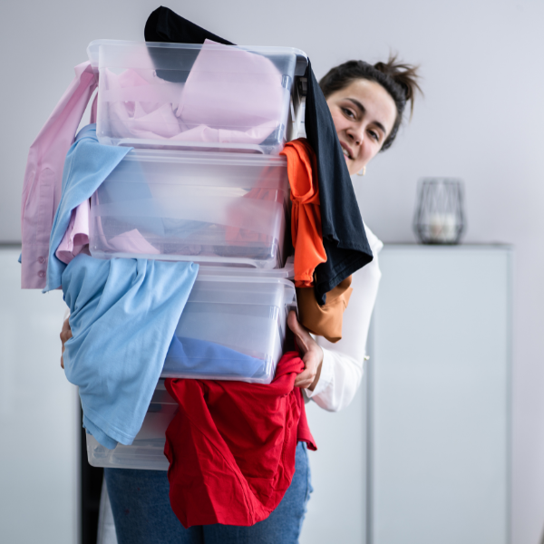 A woman carrying three clear plastic boxes full of clothes