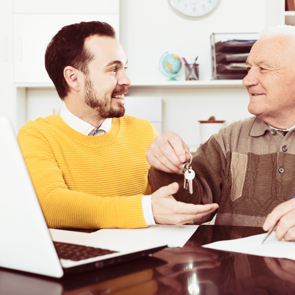 Older man hanging over house keys to younger man after selling house