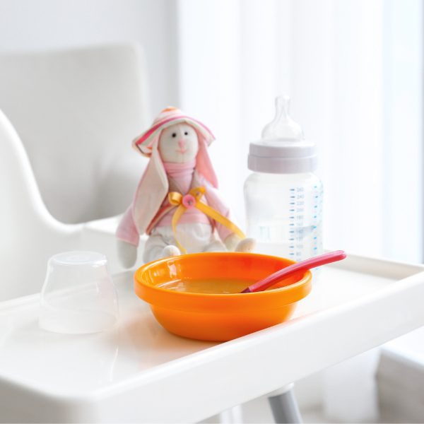 Baby highchair with bottle, cuddly rabbit toy and orange bowl