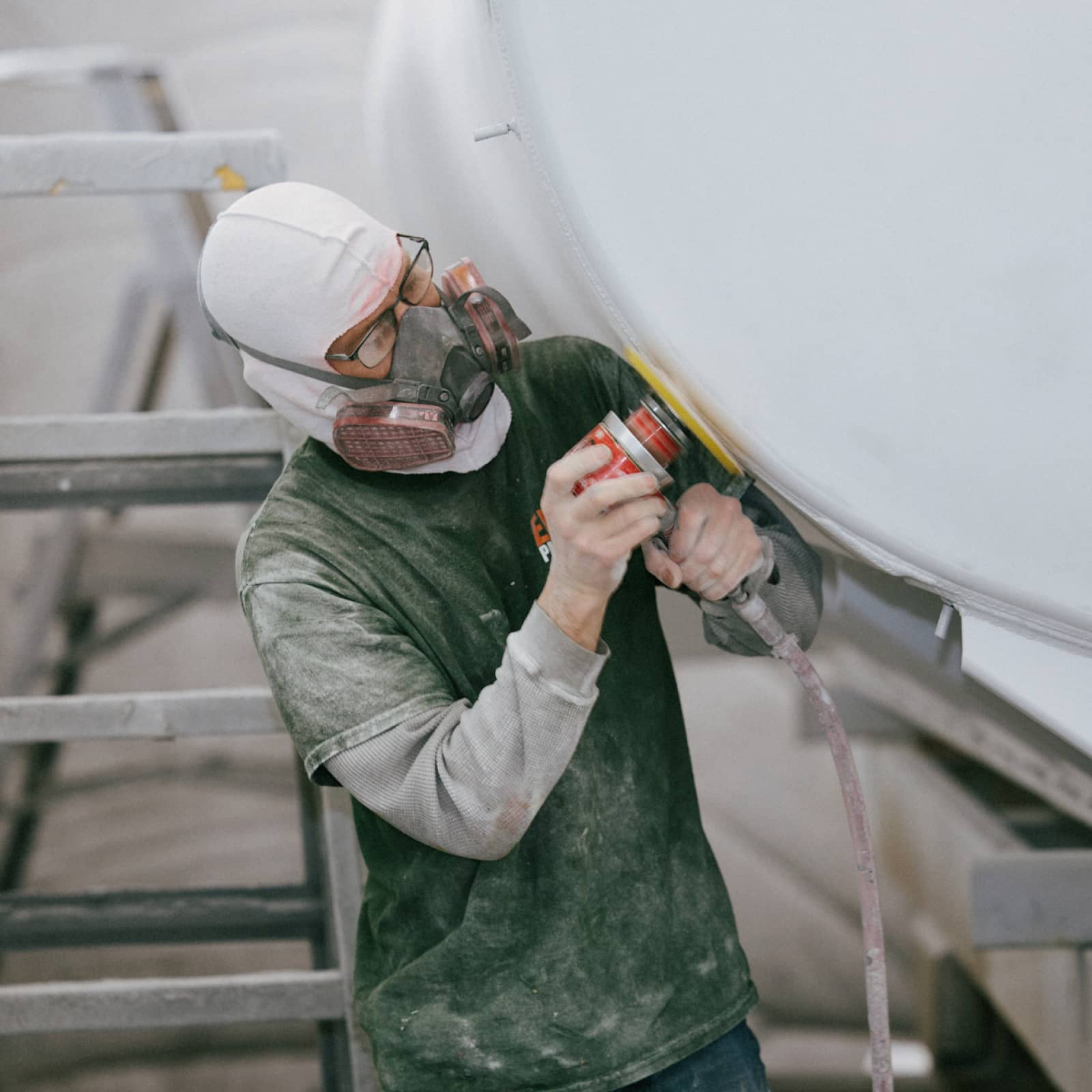 An employee wearing PPE and sanding a surface to prep for paint