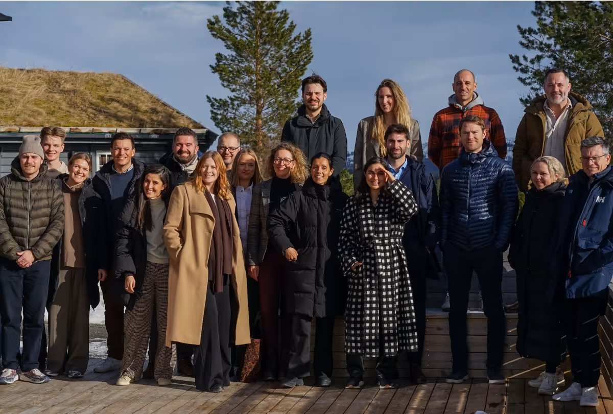 Group of twenty people standing together outdoors on a wooden deck with trees and a house in the background.