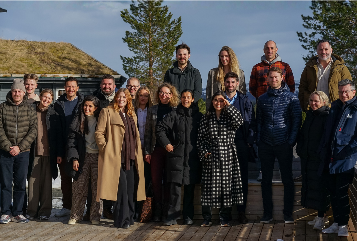 Group of twenty people standing together outdoors on a wooden deck with trees and a house in the background.