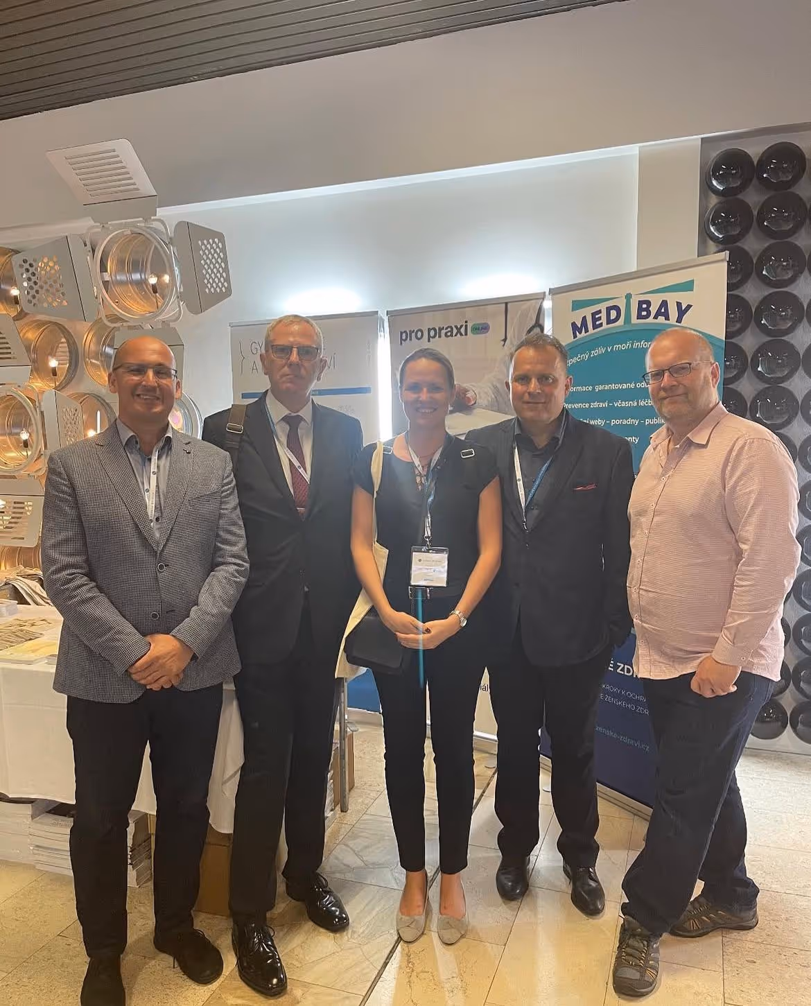 Žena a čtyři muži stojící před reklamním bannerem na konferenci