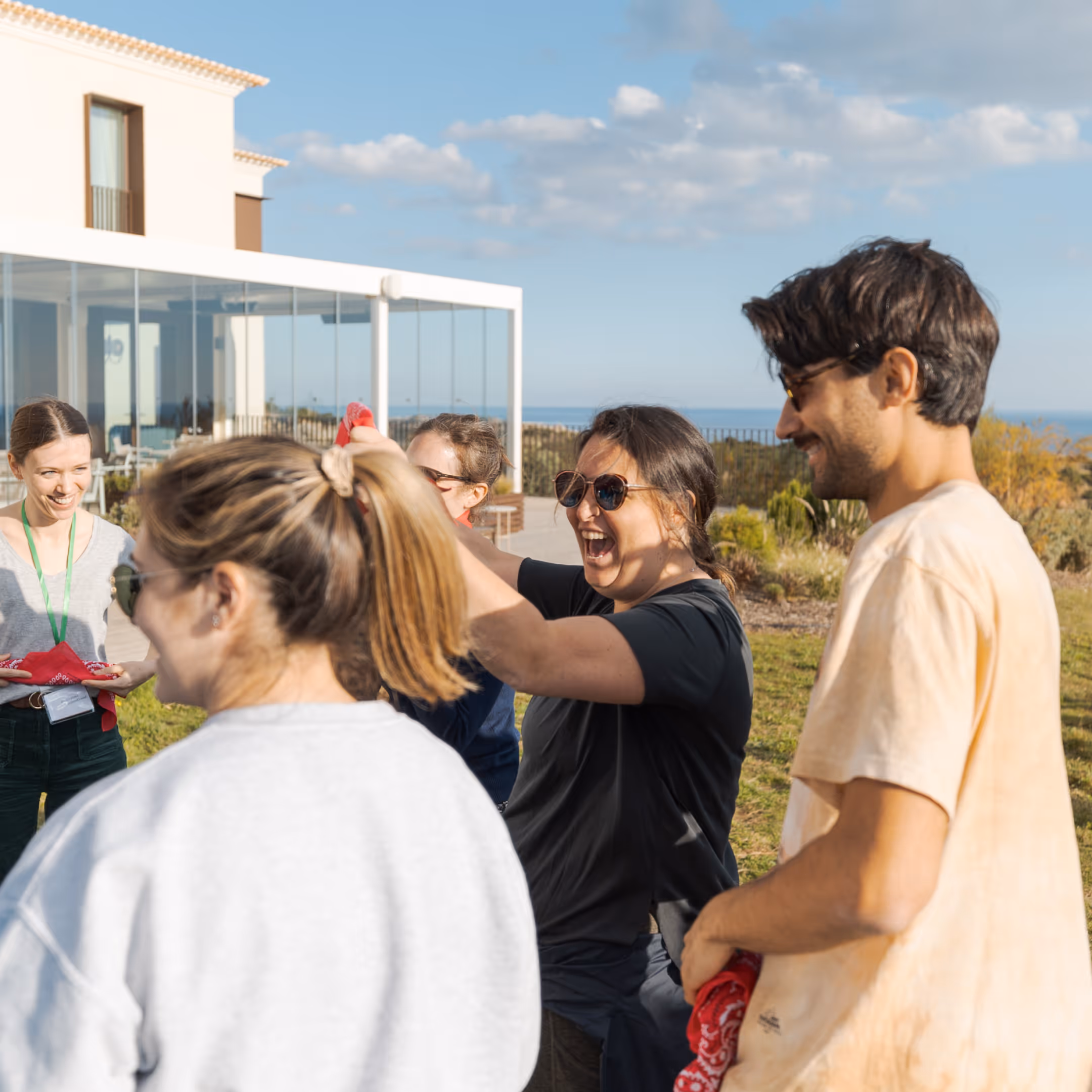 Group of five adults enjoying an outdoor gathering near a modern building with a scenic background.