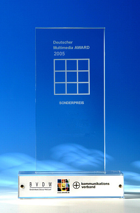 A clear glass award with a white base, inscribed “Deutscher Multimedia AWARD 2005 Sonderpreis,” stands against a blue background. Logos of BVDW and Kommunikations Verband are visible on the base.