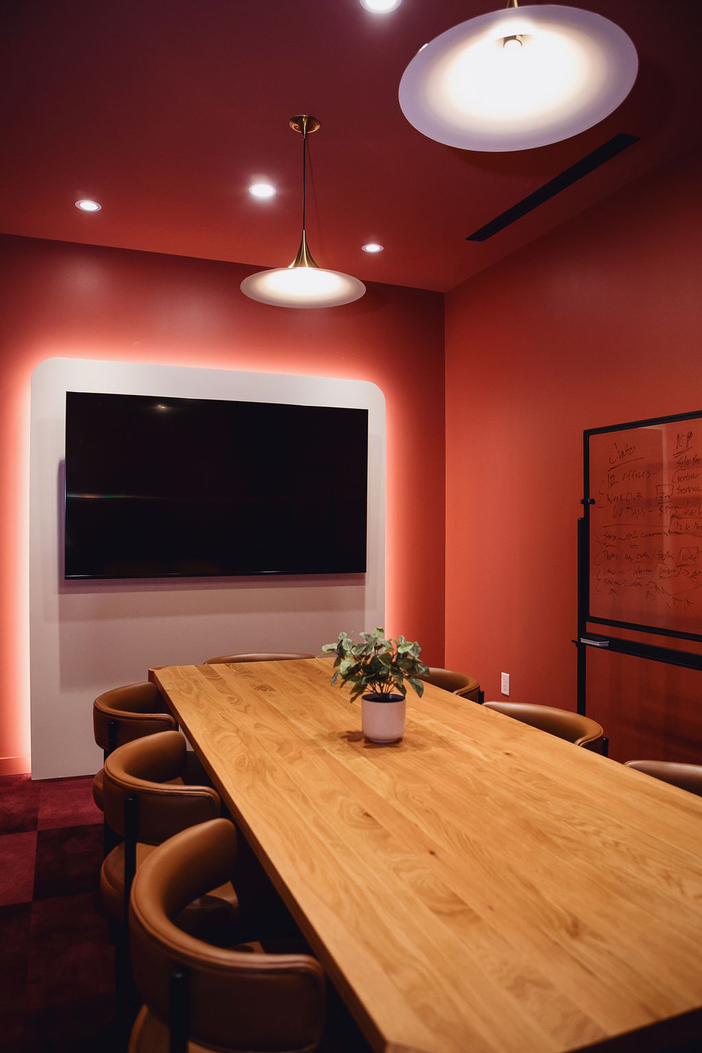 Meeting room at Junto House with a long wood table, whiteboard wall, and pendant lighting.