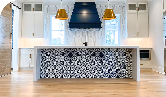 Modern kitchen interior featuring a decorative tile island, gold pendant lights, and white cabinetry for a contemporary design.