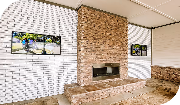 Outdoor patio with stone tile installation featuring a central stone fireplace and two wall-mounted TVs, showcasing professional craftsmanship and design.