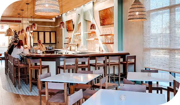 Modern commercial space with wooden flooring, featuring a bar area with high chairs, pendant lighting, and decorative wall art.