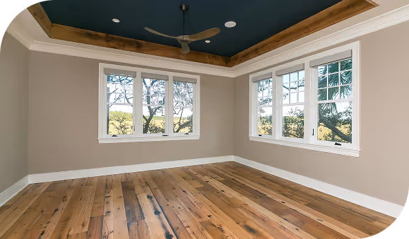 Spacious room with large windows and natural wood flooring, featuring a modern ceiling fan and neutral wall colors.