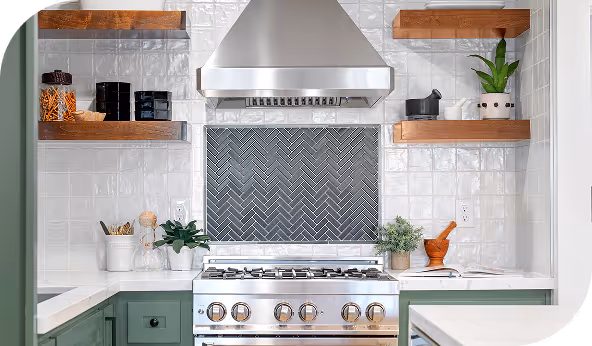 Modern kitchen with white tile backsplash in a herringbone pattern behind stove, featuring green cabinets and wooden shelves with plants and decor.