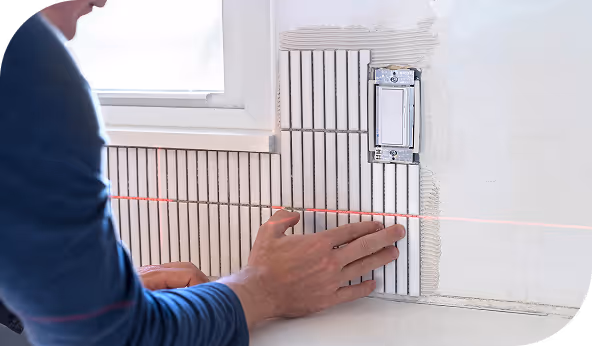 erson installing vertical tile backsplash with precision using a laser level near a light switch, showcasing expert craftsmanship in kitchen renovation.