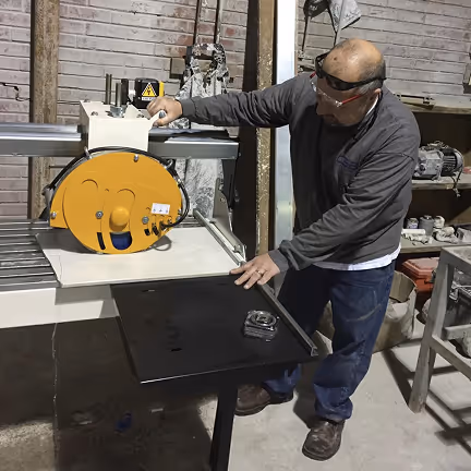 Man operating a large industrial saw in a workshop with safety goggles, surrounded by tools and equipment.