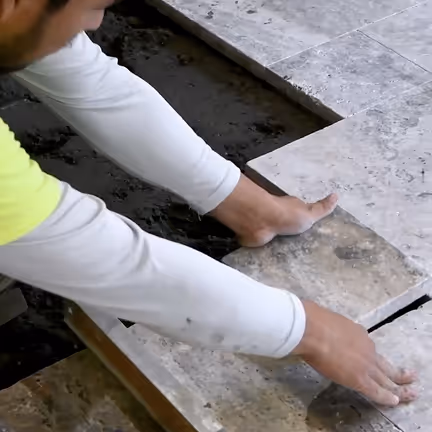 Worker installing brown exterior tiles with precision, showcasing detailed craftsmanship and tile alignment.