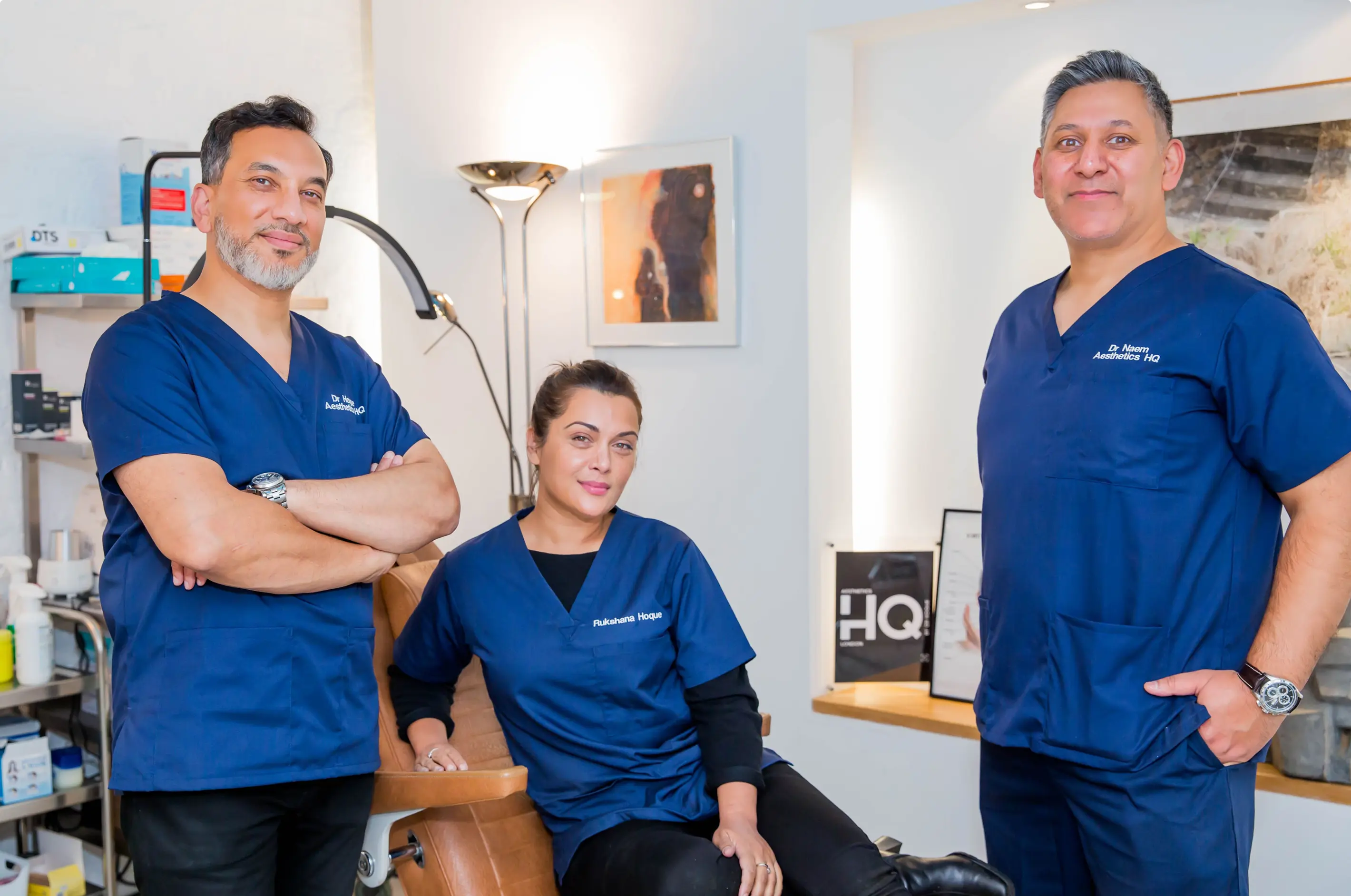 Three medical professionals in blue scrubs posing in a clinical setting with certificates and medical supplies in the background.