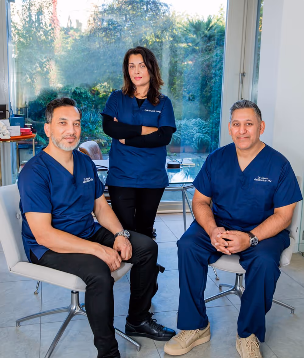 Three medical professionals in navy blue scrubs pose in a bright room with a large window showing a garden outside.
