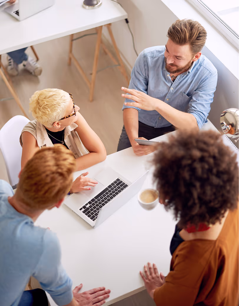 Small group gathered around a table discussing work with a laptop open in the center.