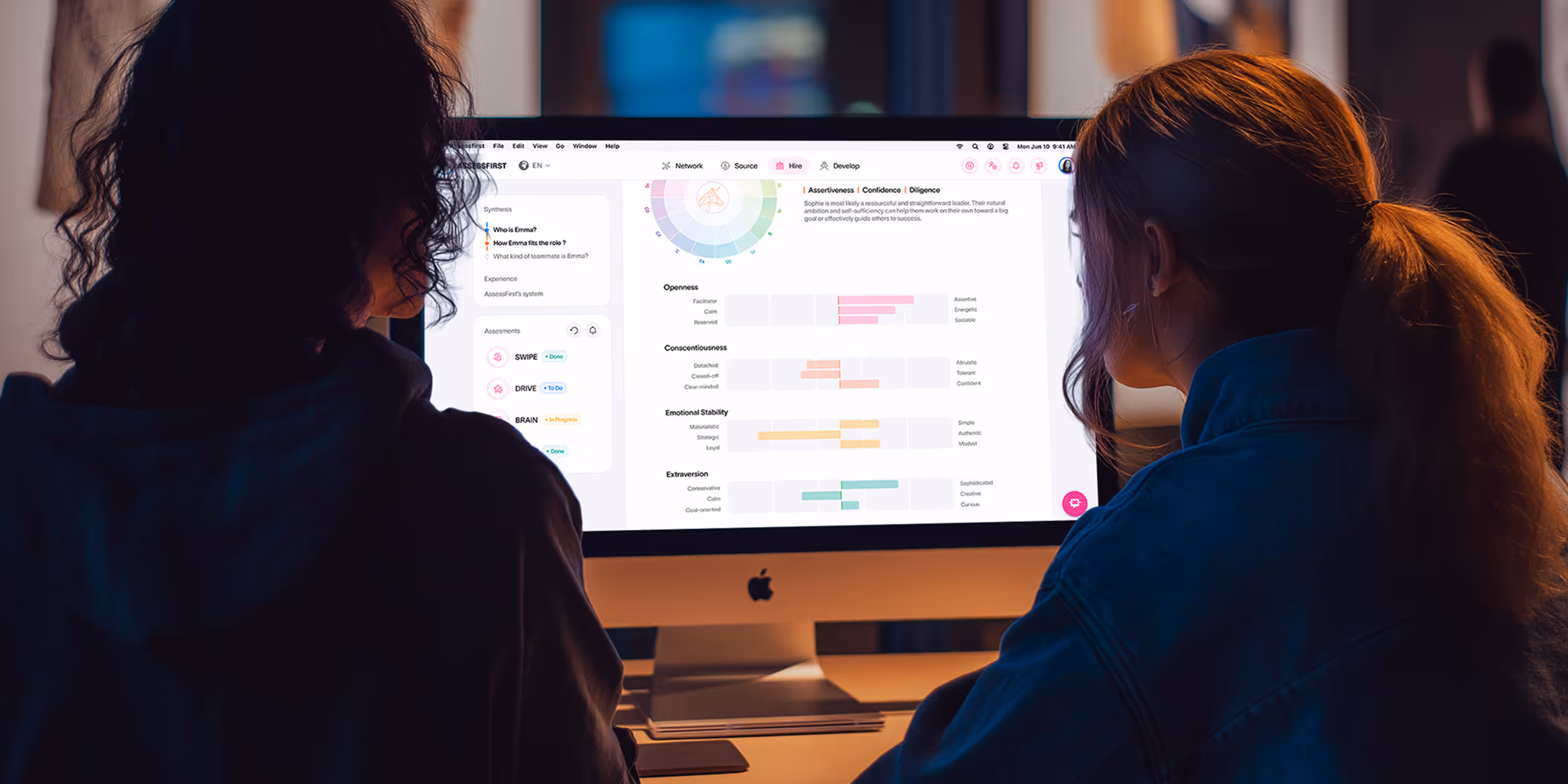 Two people sitting in a dim room reviewing detailed assessment results on a desktop computer.
