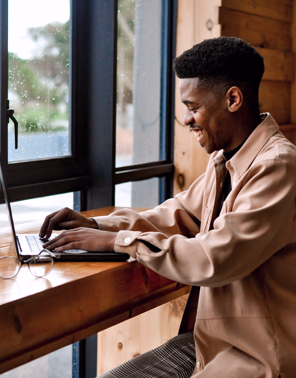 Person working alone on a laptop at a wooden counter next to a window in a relaxed workspace.