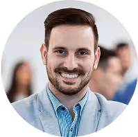 Lächelnder Mann im grauen Sakko und blauer Hemd vor verschwommenem Hintergrund.