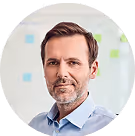 Ein lächelnder Mann in Hemd vor einer Wand mit bunten Notizzetteln.