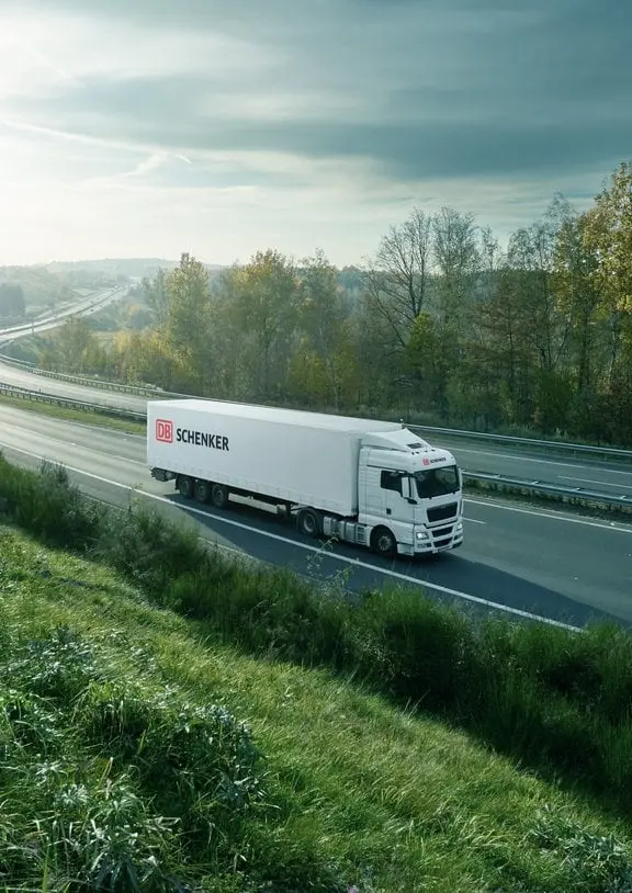 Stacks of DB Schenker shipping containers arranged in rows at a logistics yard under a clear blue sky.