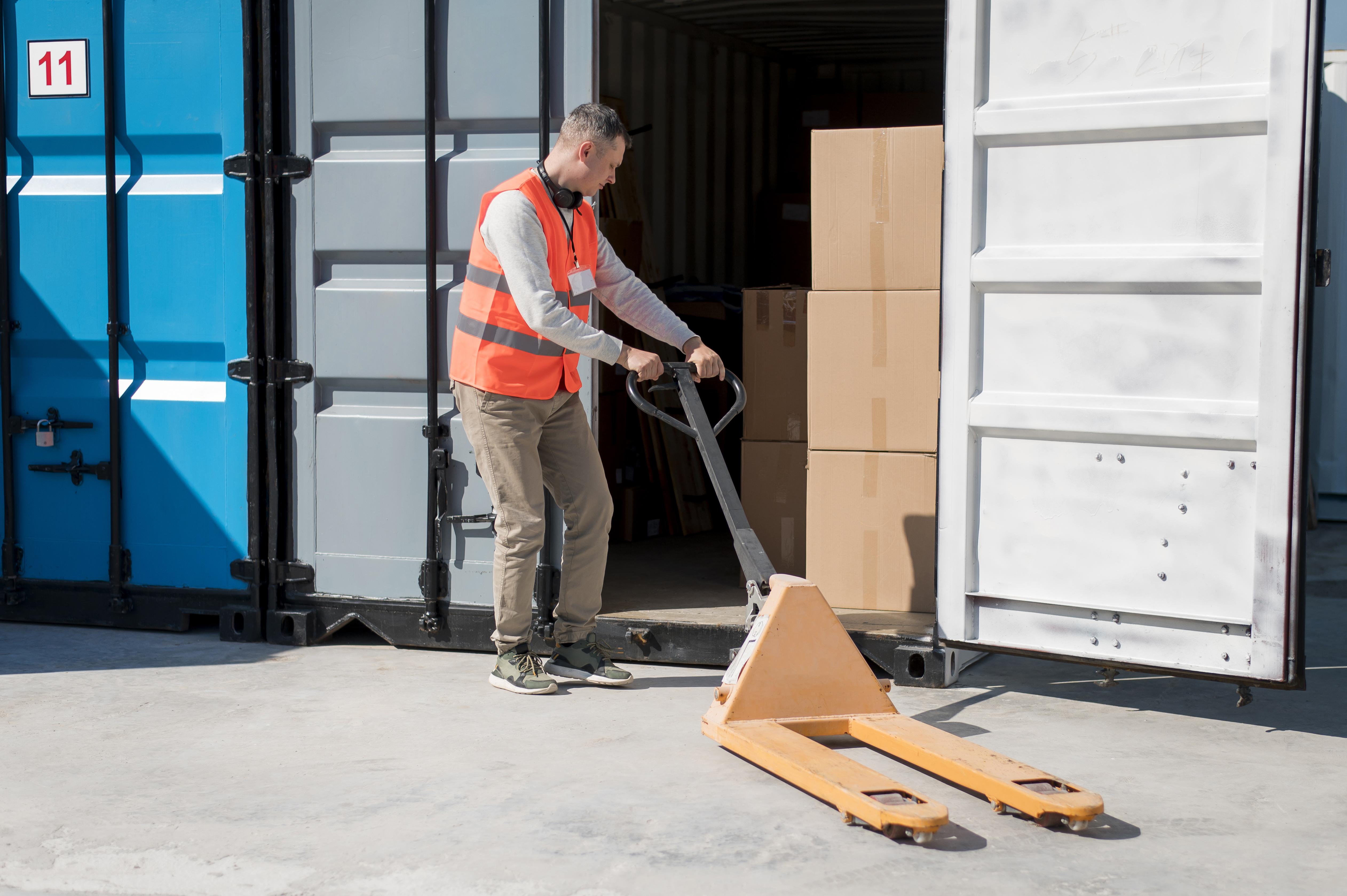 Warehouse worker in safety gear operating an electric pallet jack inside a logistics facility.