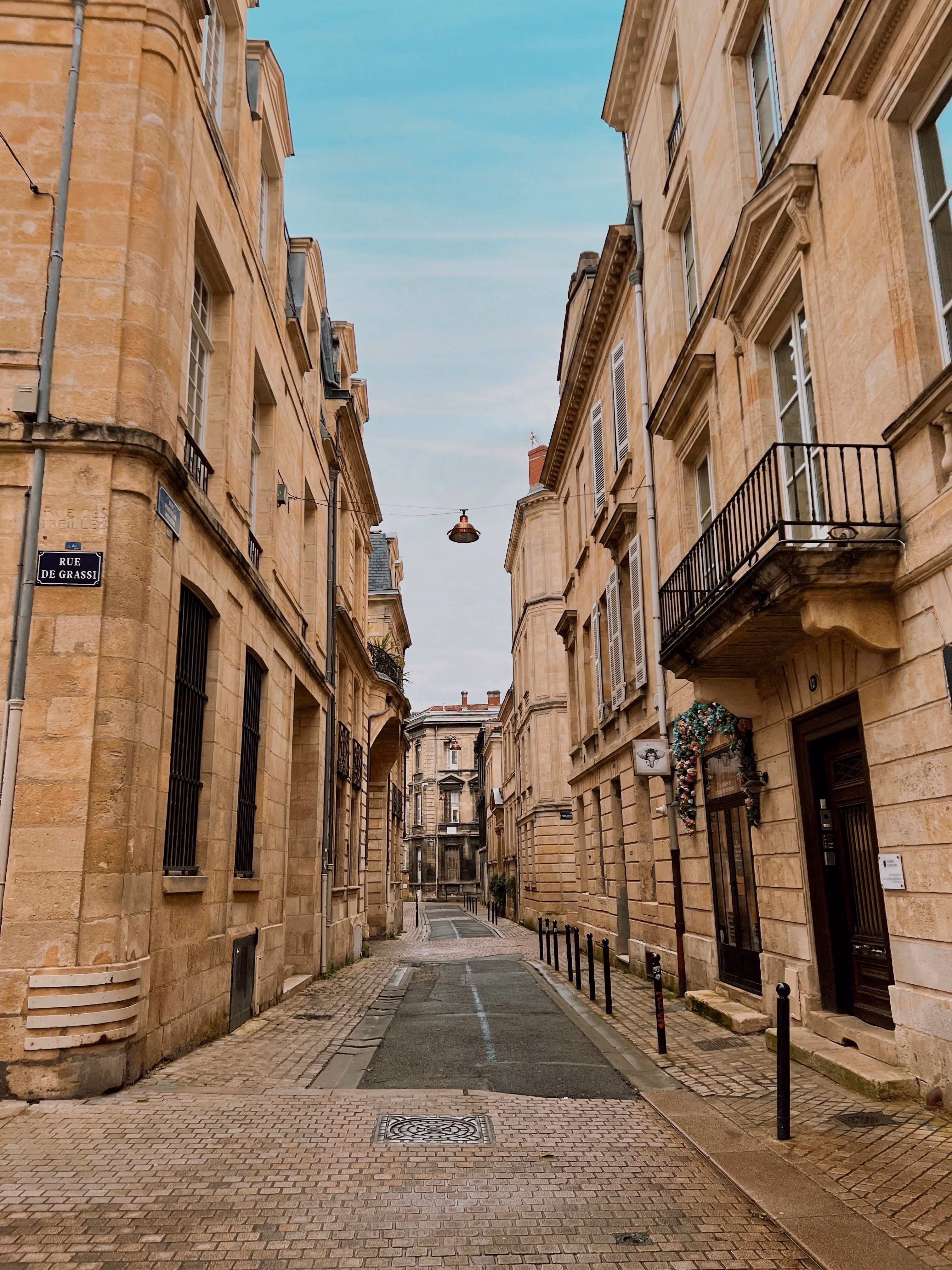 Rue pavée étroite bordée de bâtiments en pierre avec balcons et une enseigne fleurie.